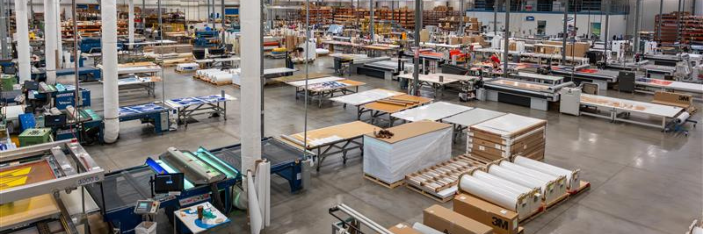 Wide shot of a high-tech industrial manufacturing facility floor with large-scale printing equipment and clean architectural lines under cool lighting